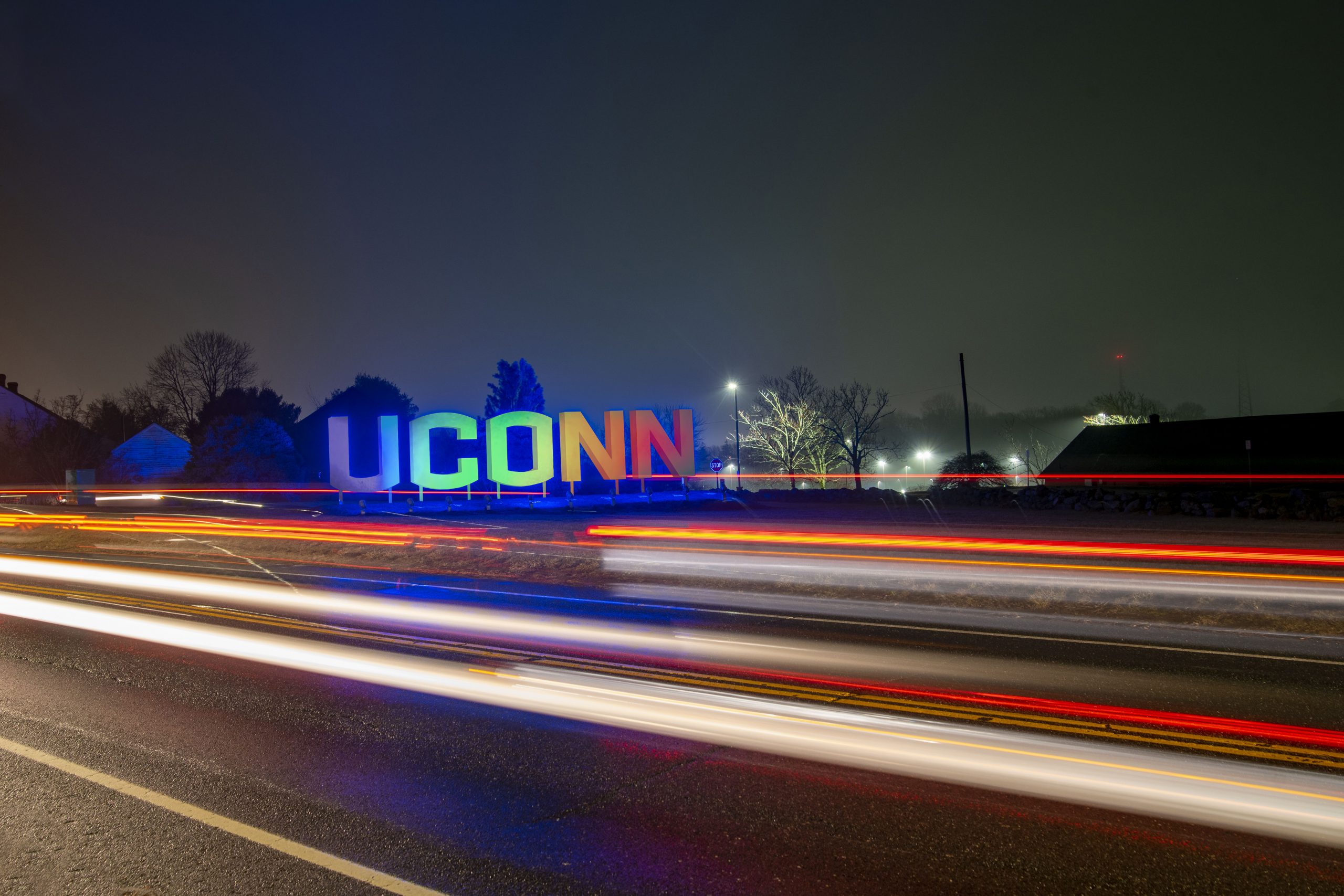 Large UConn sign lit up at night with light trails from car traffic. Feb. 6, 2020. (Sean Flynn/UConn Photo)